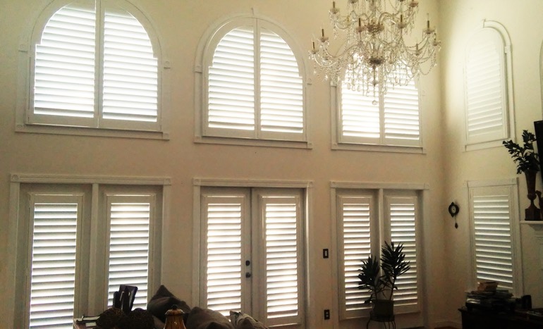 Television room in open concept Houston home with plantation shutters on high ceiling windows.