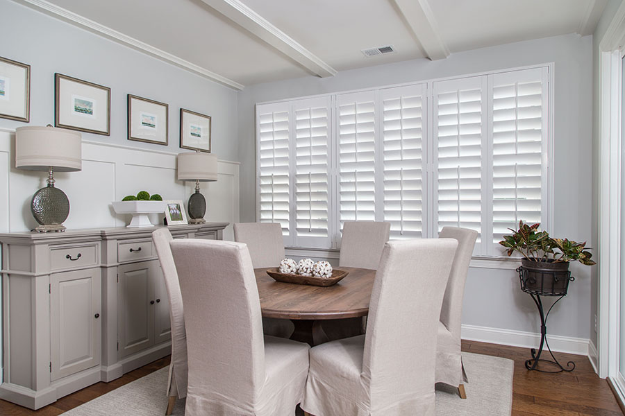White Polywood shutters on a large picture window within a medium-sized dining room.
