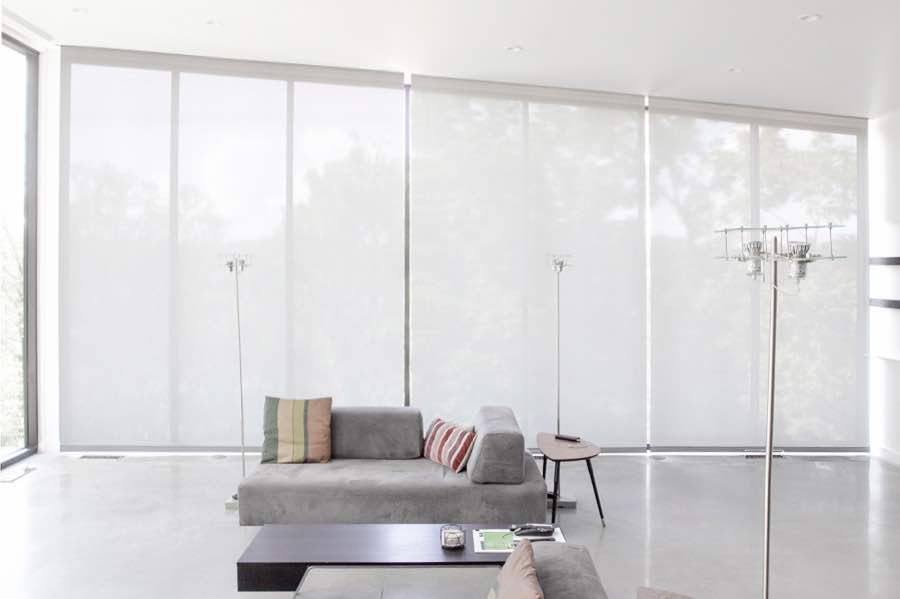 Motorized window shades make controlling natural light effortless in your Houston great room. White motorized shades on a wall of tall great room windows