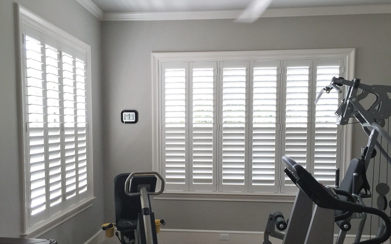 Weatherstripping window treatments are especially important in rooms with windows on more than one wall. Houston fitness room with shuttered windows.