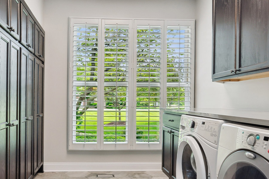 Find the perfect level of natural light for your Houston laundry room with interior shutters. White Polywood shutters letting light through a laundry room window