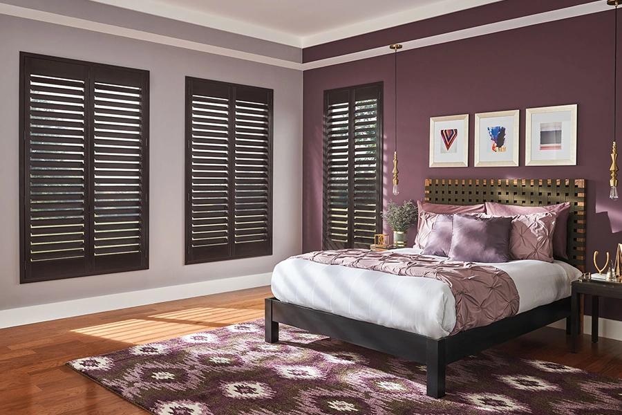Dark wood ovation shutters within three windows inside a bedroom